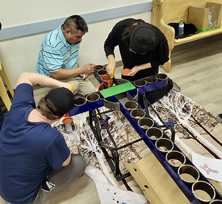 A metal cross is being painted by three men.