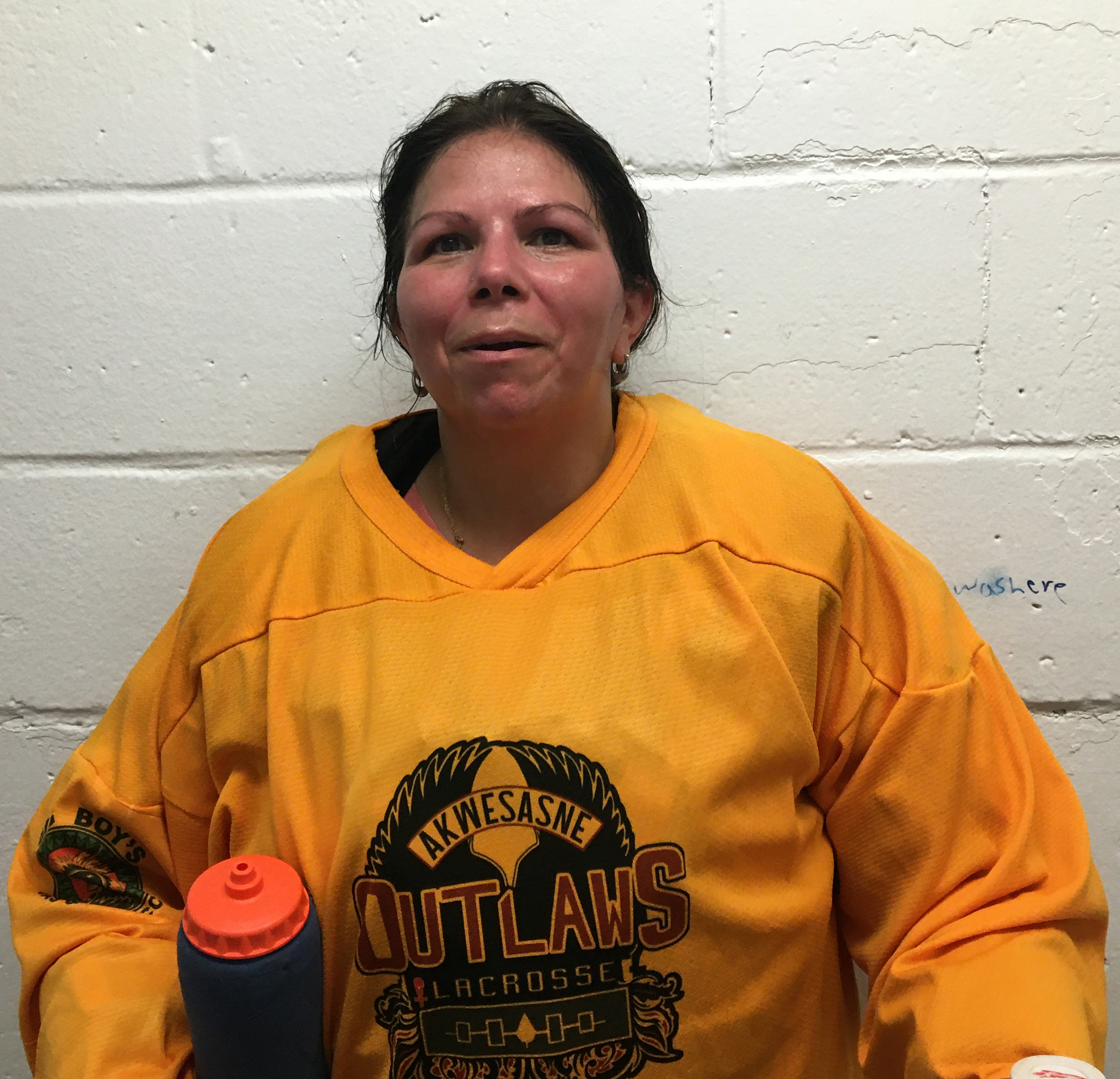 A woman wearing a sports jersey stands against a white block wall.