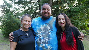 Three smiling people are standing in a forest, close together as friends.