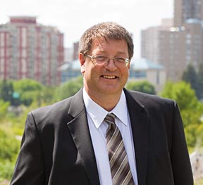 Man in a suit standing in front of a city-scape.