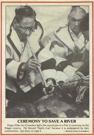 Men in Hudson's Bay blanket jackets sit cross-legged in a tipi. One man has a long tradition pipe that he is performing a ceremony with.