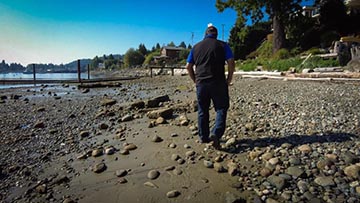 A man walks alone on a stoney beach.