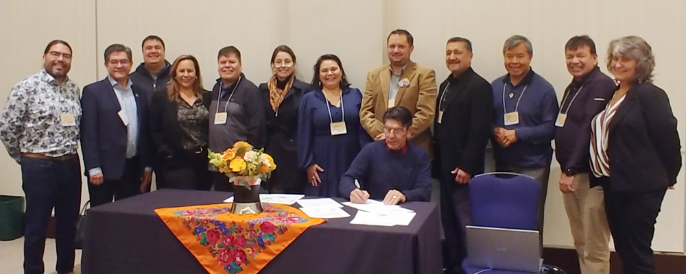 A group of people. One is signing a document at a table.