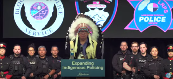 Tsuut’ina Nation Chief Roy Whitney Onespot stands wearing a headdress in from of police members