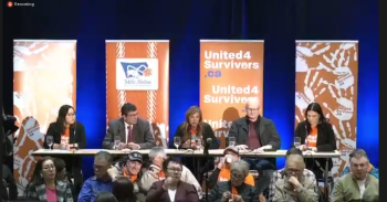 Five people sit at a long table in front of vertical orange panels with writing on them, including United4Survivors.ca and handprints with that same website printed on them.