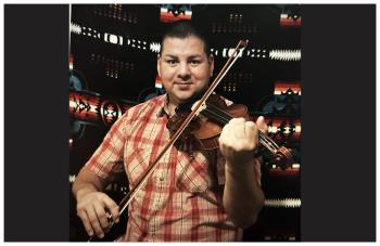 Adam Daigneault wears a red checked short-sleeved shirt. He holds a fiddle under his chin and a bow to the strings. He is standing in front of a blanket with a geometric design. He is starring smiling.