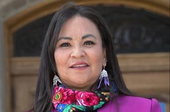 A woman stands outside a legislature building and looks at the camera.