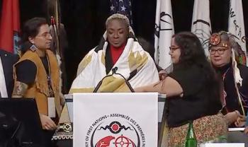 A woman looks emotional as she stand before a microphone after she was wrapped in a blanket. 