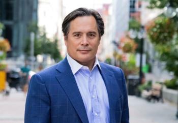 A man in a blue suit is on a tree covered city street. He looks at the camera.