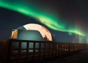 A dome shines against a dark sky lit up by northern lights.