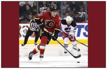 A hockey player with a Calgary Flames uniform on charges up the ice with a puck.