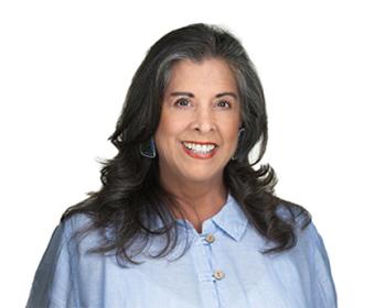 A head and shoulders shot of a woman with longish brown hair hanging over her shoulders. She wears a blue blouse.