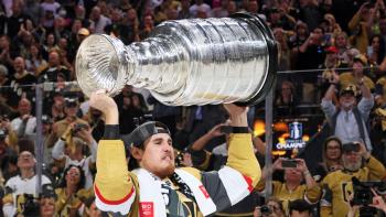 A beard man in a hockey uniform raises the Stanley Cup above his head.