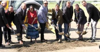 People line up with shovels digging into the ground for a ceremonial sod turning.