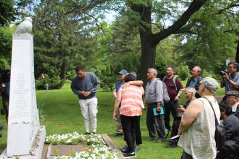 People gather around a stone monument in a cementary.