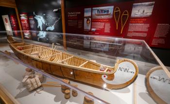 A birchbark canoe is displayed in a case.