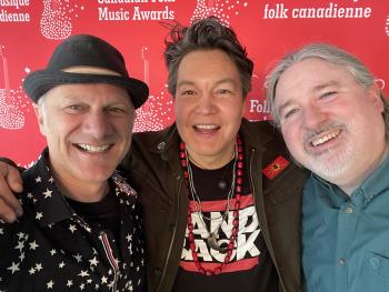 Three men pose with wide smiles for the photo against a red background.