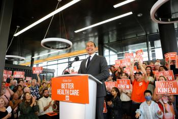 A man stands at a podium surrounded by cheering people displaying NDP election signs.