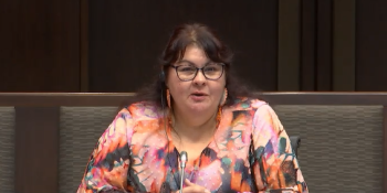 A woman in sits in front of a microphone answering questions.