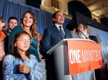 A man stands at a podium smiling victoriously. A woman stands beside him with children around them.