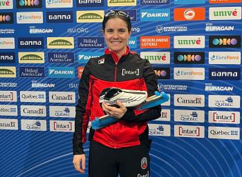 A young woman stands smiling in front of a panel covered in sponsors' plaques.