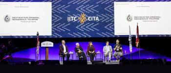 People sit on chairs on a large conference stage underneath banners that read Destination Original International Tourism.