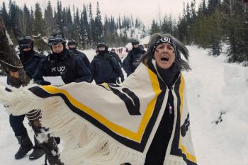 A woman turns, her woven blanket shawl swings out. She is angry, frightened and yelling out toward the camera.