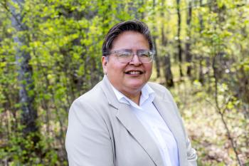 Photo is of a woman standing in an outdoor setting amongst the trees.