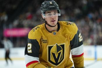 A man in a black helmut and gold coloured jersey with the Golden Knights hockey team logo on it skates on the ice inside a stadium rink.