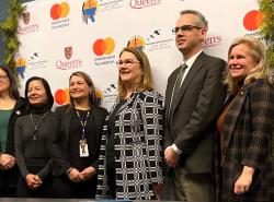 Six people line up in front of a banner with logos on it for a photo.