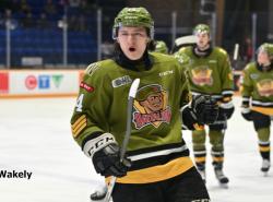 A teen hockey player in a moss green jersey on the ice. He pumps his glove in a celebratory gesture.