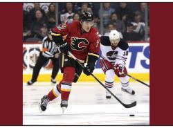 A hockey player with a Calgary Flames uniform on charges up the ice with a puck.