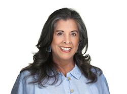 A head and shoulders shot of a woman with longish brown hair hanging over her shoulders. She wears a blue blouse.