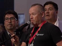 Three men stand around a microphone.