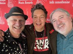 Three men pose with wide smiles for the photo against a red background.