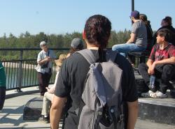 A grey-haired woman speaks to a group of people on a bridge. 