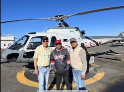 Three men stand in front of a helicopter.