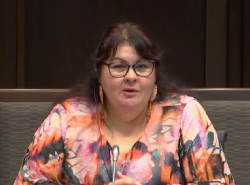 A woman in sits in front of a microphone answering questions.