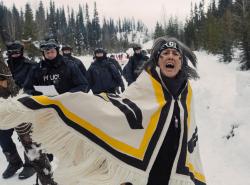 A woman turns, her woven blanket shawl swings out. She is angry, frightened and yelling out toward the camera.