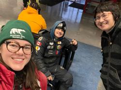 Three people bundled up for cold temperature are waiting in an airport. They smile at the camera.