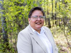 Photo is of a woman standing in an outdoor setting amongst the trees.