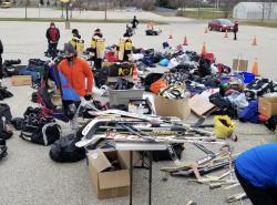 Hockey equipment is scattered across a parking lot as people go through and choose what they need for their children's hockey bags.