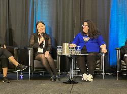 Sitting on chairs on a stage are four women.