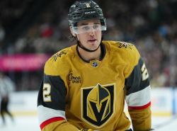 A man in a black helmut and gold coloured jersey with the Golden Knights hockey team logo on it skates on the ice inside a stadium rink.