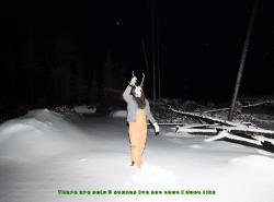 A man walks at night throug the snow. He holds a caribou skull in front of his face.
