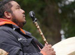 A man looks to the skies as he plays a hand drum. He is standing outdoors.