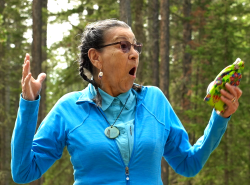 Surprise! A woman has her hands up and a look of surprise on her face. She stands amongst the trees.